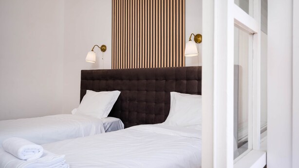 A hotel room with two beds, a dark headboard, white bedding, and two wall-mounted lamps. - Algarve Townhouse in Loulé by MGM Stays (Loulé)