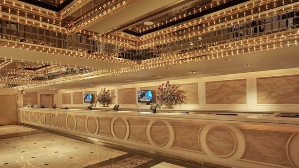 Un hall d’hôtel comprenant un comptoir d’accueil, plusieurs écrans et une composition florale décorative.