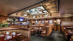 Un restaurant avec des banquettes, un bar et un plafond orné de vitraux.