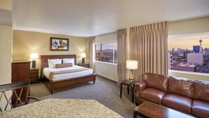 Ein Hotelzimmer mit einem Bett, einem Ledersofa, einem Schreibtisch und Blick auf eine Stadtlandschaft.