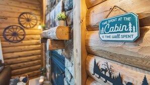 Interior de una cabaña con pared de madera, un cartel que dice 'El tiempo en la Cabaña es tiempo bien empleado' y la silueta de un ciervo y árboles.