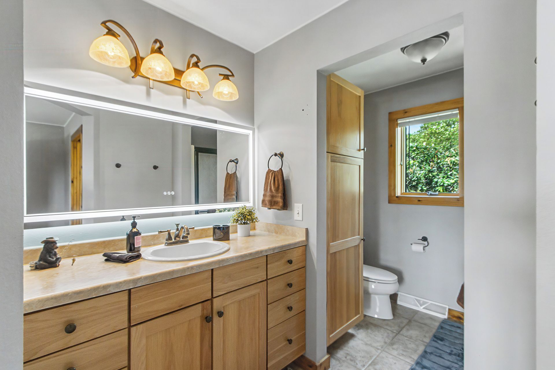 A bathroom with a large mirror, a sink, wooden cabinets, a towel rack, and a window.