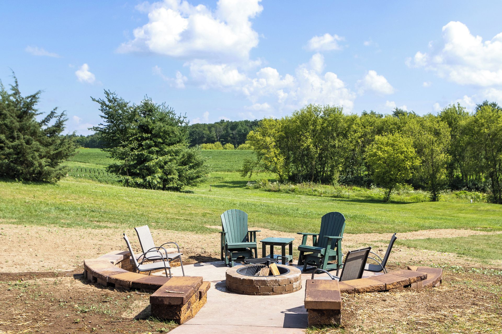 An outdoor seating area with chairs and a fire pit, surrounded by a grassy field and trees.