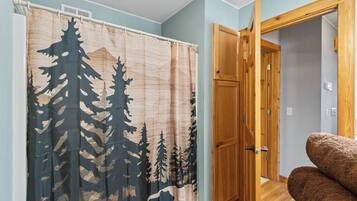 Una habitación con cortina de ducha con estampado de bosque, una puerta de madera y una silla marrón.
