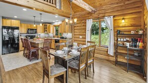 Una cocina amplia con armarios de madera, un comedor con mesa dispuesta para cuatro personas y vistas al exterior a través de un ventanal grande.
