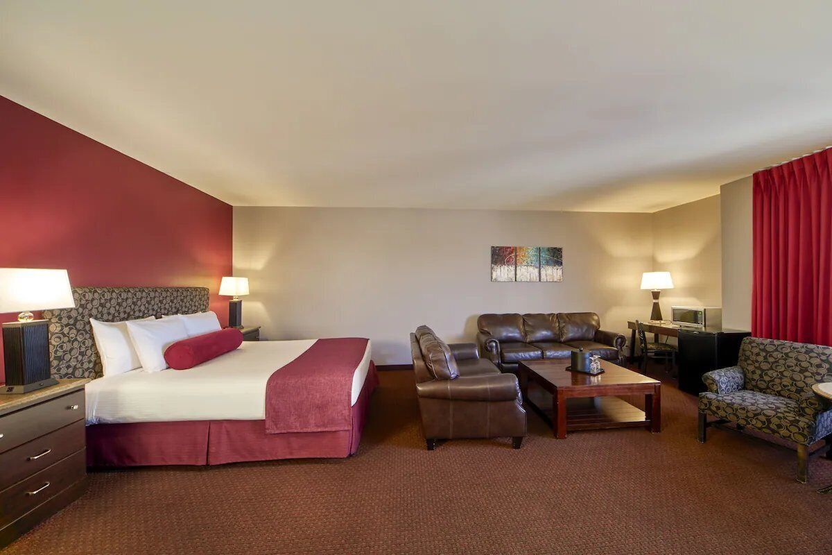 Ein Hotelzimmer mit einem Bett, zwei Ledersofas, einem Couchtisch und einem Schreibtisch mit einer Lampe.