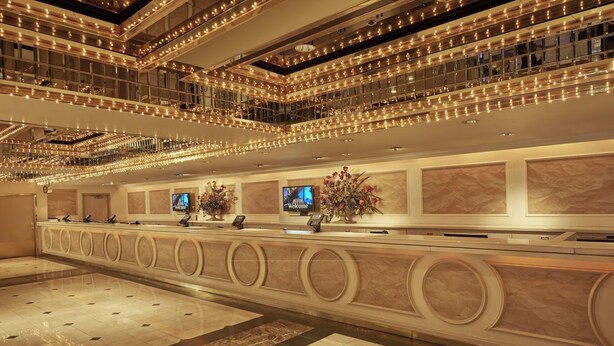 Hall dell'hotel con reception, diverse schermate e una composizione floreale decorativa.