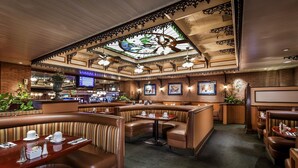 Un ristorante con cabine, un bar e un soffitto decorato con un motivo in vetro colorato.