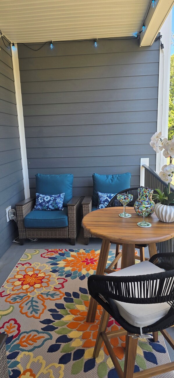 A covered patio area with wicker furniture, a wooden table, and a colorful rug. - New Condo Rehoboth 3BR w/4 E-Bikes, Pool + Gym (Rehoboth Beach)