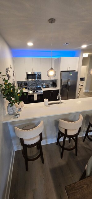 A modern kitchen with a central island, stainless steel appliances, and a hanging light fixture. - 2 Minute Walk to Schellville + Outlets, 3 BR + 2 Bath Luxury Condo, Gym, E-bikes (Rehoboth Beach)