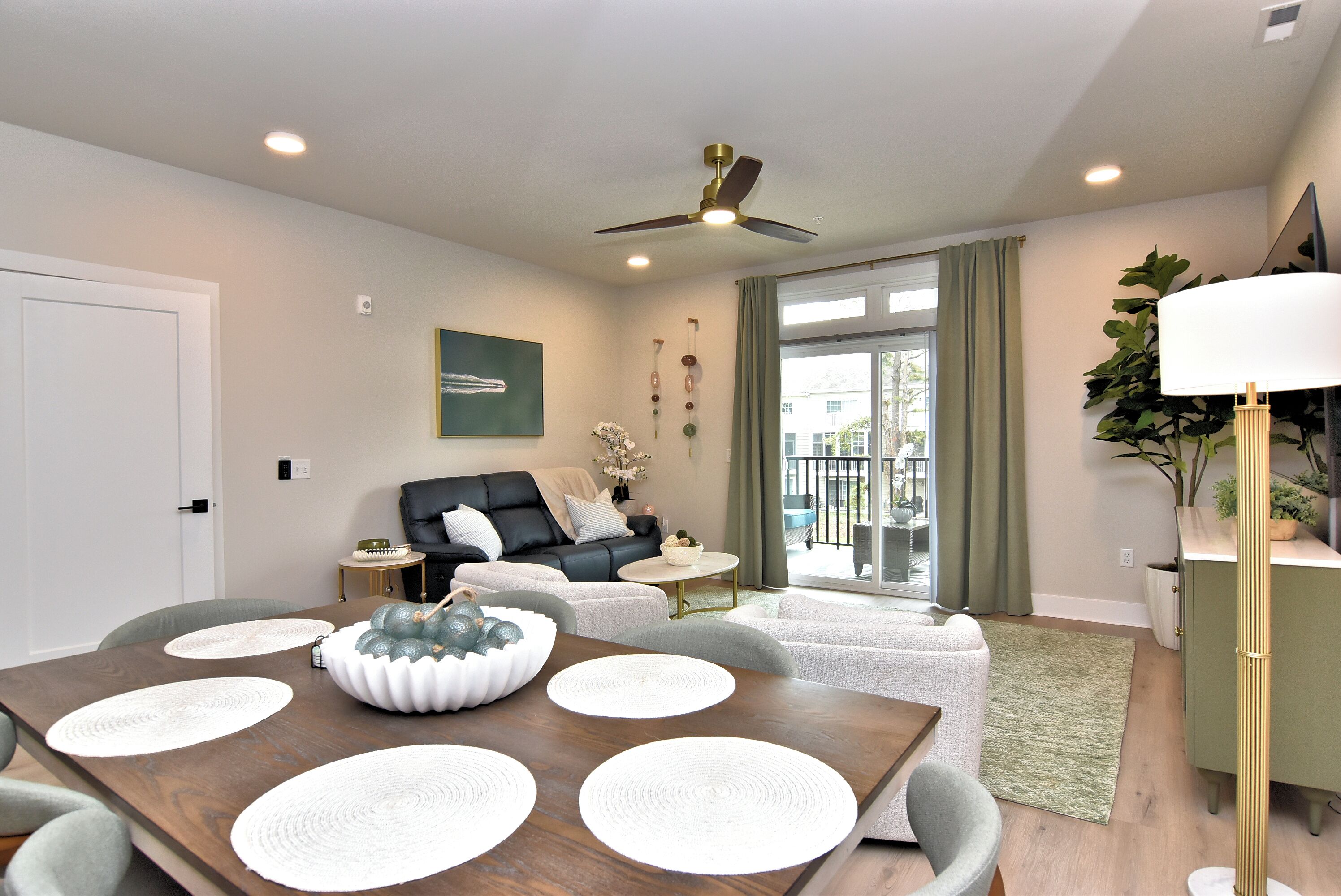 A modern living room with a dining area, a ceiling fan, a sofa, a coffee table, and a view through a glass door.