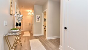 A hallway with a marble table, a potted plant, a framed picture, and a door leading to another room. - New Condo Rehoboth 3BR w/4 E-Bikes, Pool + Gym (Rehoboth Beach)