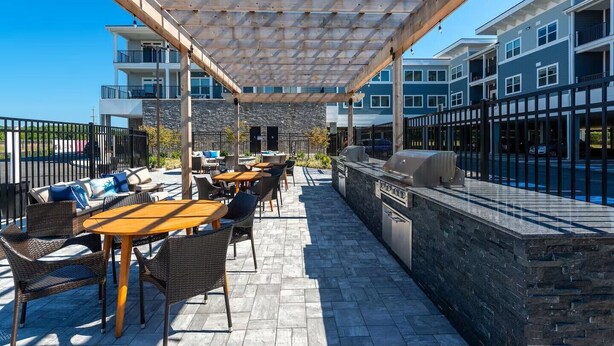 An outdoor patio with tables and chairs, a grill, and a stone wall. - New Condo Rehoboth 3BR w/4 E-Bikes, Pool + Gym (Rehoboth Beach)
