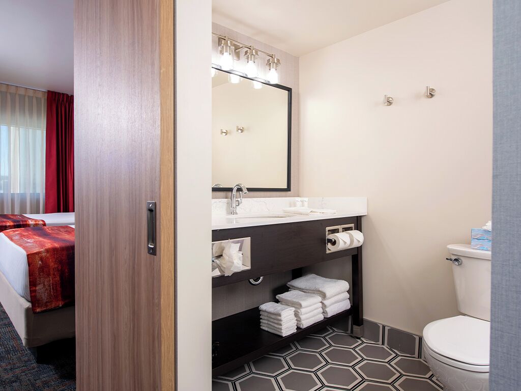 A hotel bathroom with a large mirror, a sink, a toilet, and a shower area.