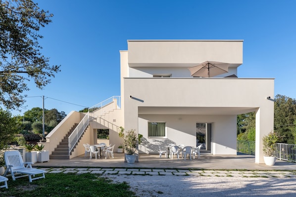 A modern two-story building with a staircase, outdoor seating area, and potted plants.