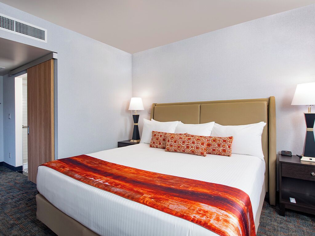 Habitación de hotel con cama, dos mesitas de noche, lámpara y aire acondicionado.