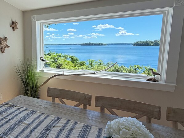 Un coin repas avec vue sur un lac, visible à travers une fenêtre, comprenant une table en bois et des chaises.