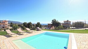 A swimming pool with lounge chairs, a stone deck, and a view of the sea and mountains. - Villa Merimonti The horizon between sea and mountains (Érétrie)