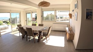 A spacious dining area with a large table and chairs, large windows with a view, and a radiator. - Villa Merimonti The horizon between sea and mountains (Érétrie)