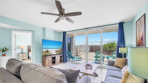 Sala de estar com sofá, mesa de centro e televisão. Tem uma varanda com vista para a praia.