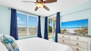 Quarto com cama, ventoinha no teto, penteadeira e uma janela grande com cortinas.