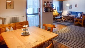 Une table à manger en bois avec des chaises, un radiateur, une bibliothèque, un canapé et une lampe.