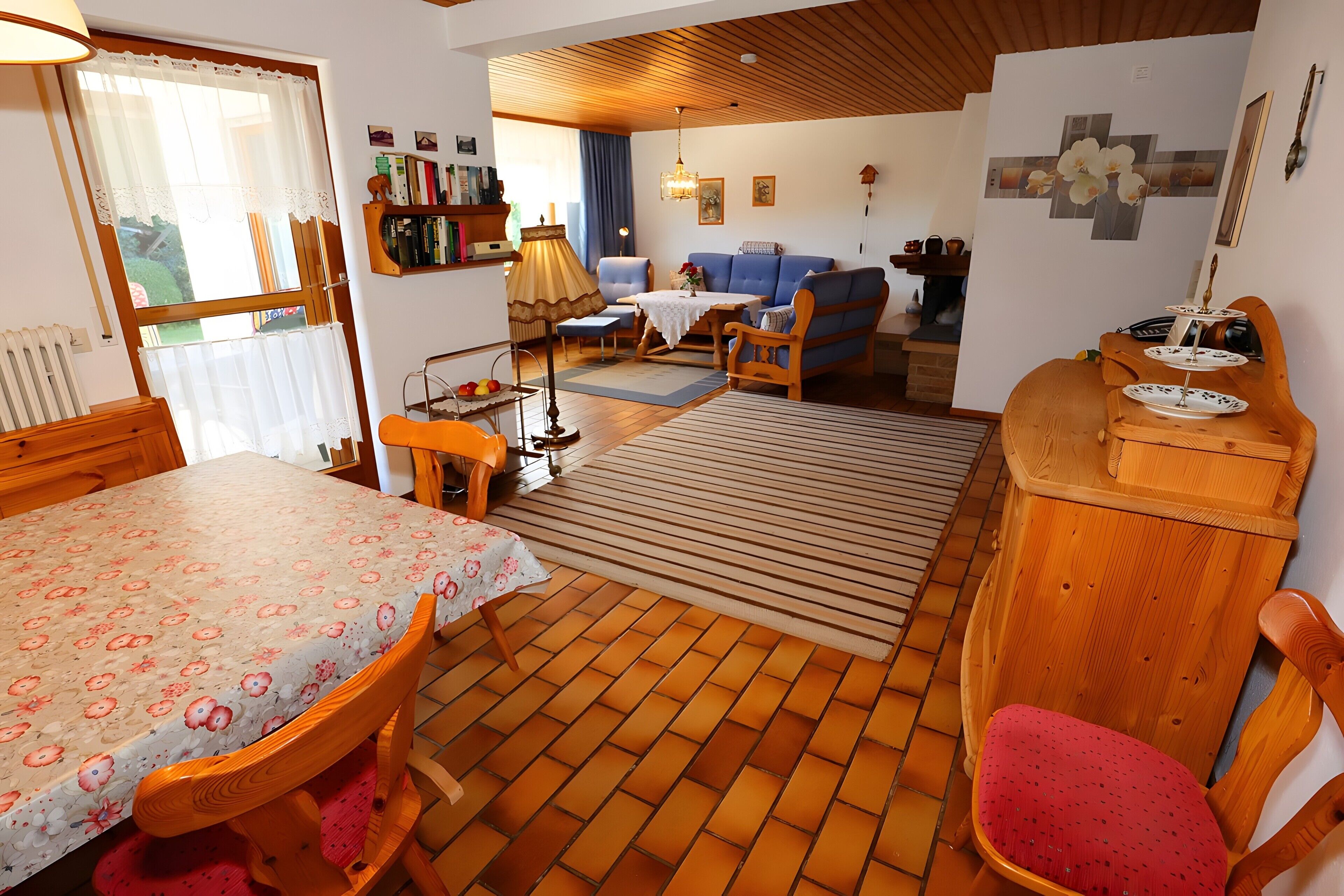 Una habitación con una mesa de comedor, sillas, un sofá, un armario de madera y un tapete estampado.