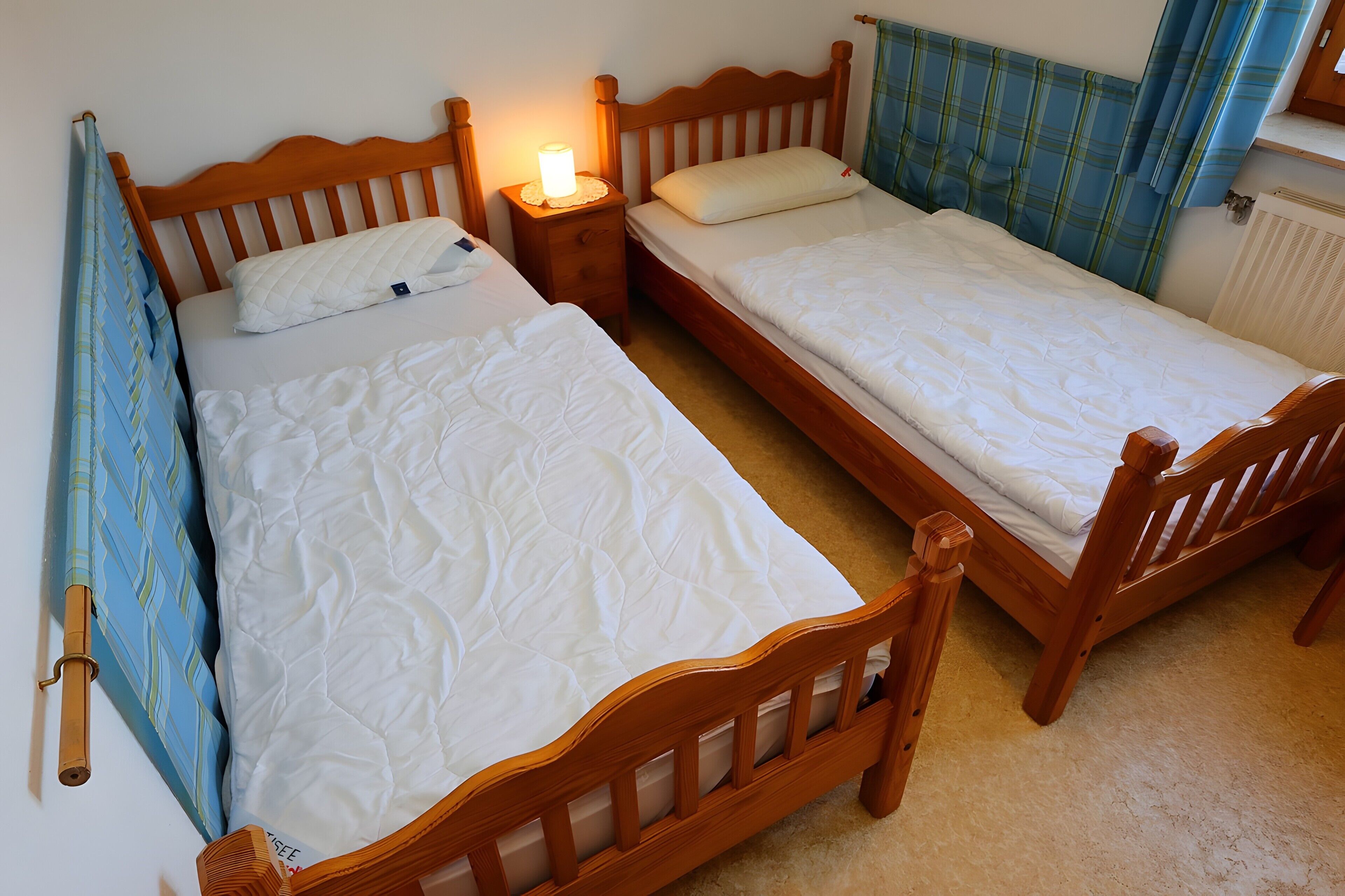 Une chambre à coucher avec deux lits en bois, une table de chevet avec une lampe et une fenêtre avec des rideaux.