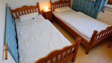 Une chambre à coucher avec deux lits en bois, une table de chevet avec une lampe et une fenêtre avec des rideaux.