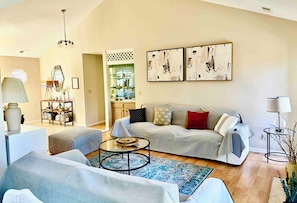 A living room with a sofa, armchairs, a coffee table, and artwork on the wall.