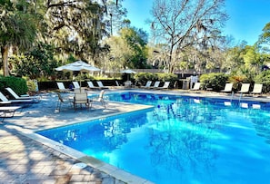 A swimming pool with lounge chairs and umbrellas, surrounded by trees and greenery.