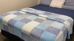 A bed with a blue and white quilt, a dark blue mattress, and a plaid pillow. - Unit 7 Beach Retreat | Walk to Shore | BBQ + Fire Pit (Wasaga Beach)