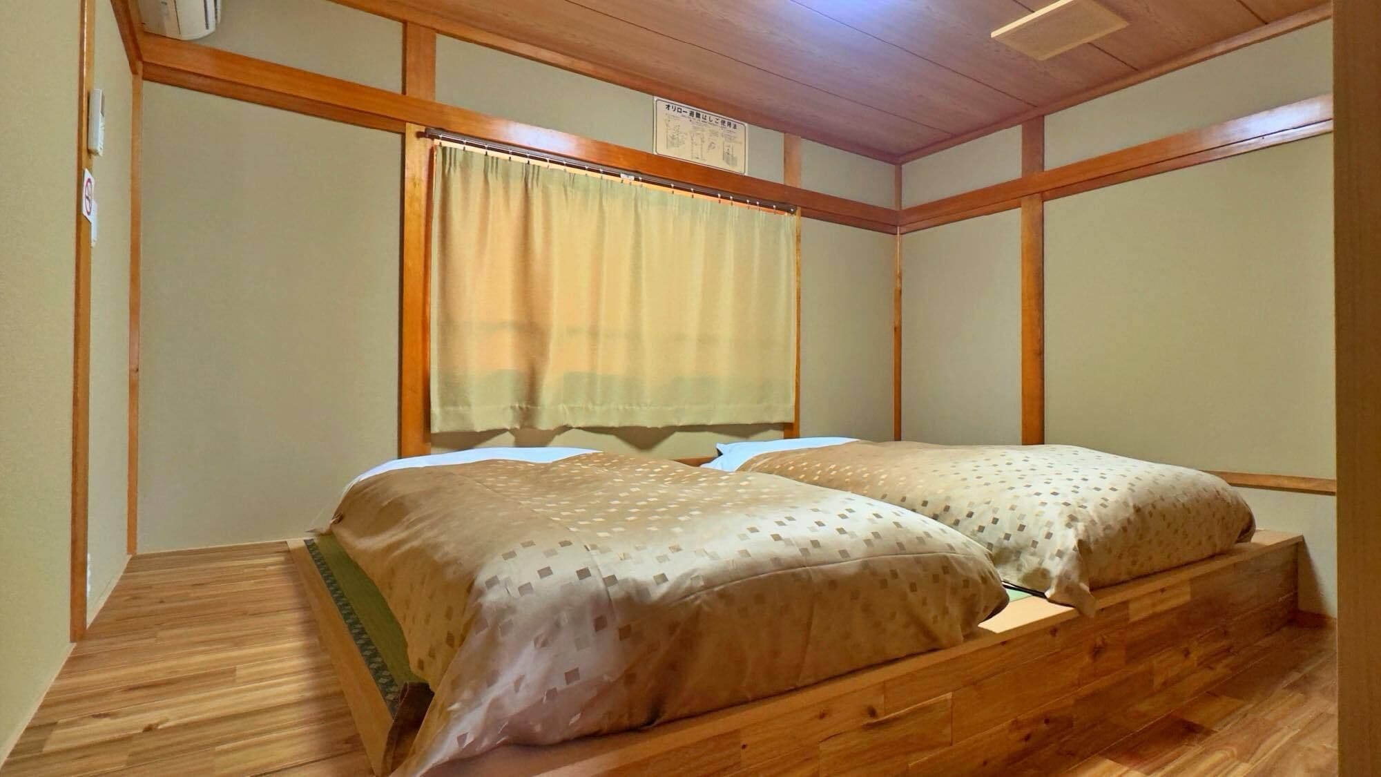 A room with a wooden bed frame, two beds, a window with a curtain, and a ceiling fan.