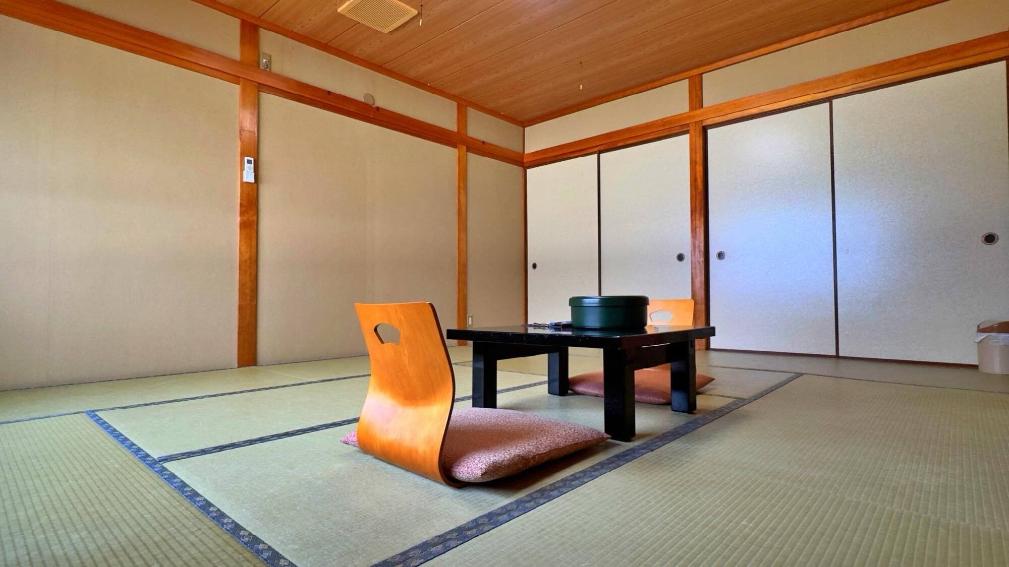 A traditional Japanese room with tatami flooring, a low table, a cushion, and sliding doors.