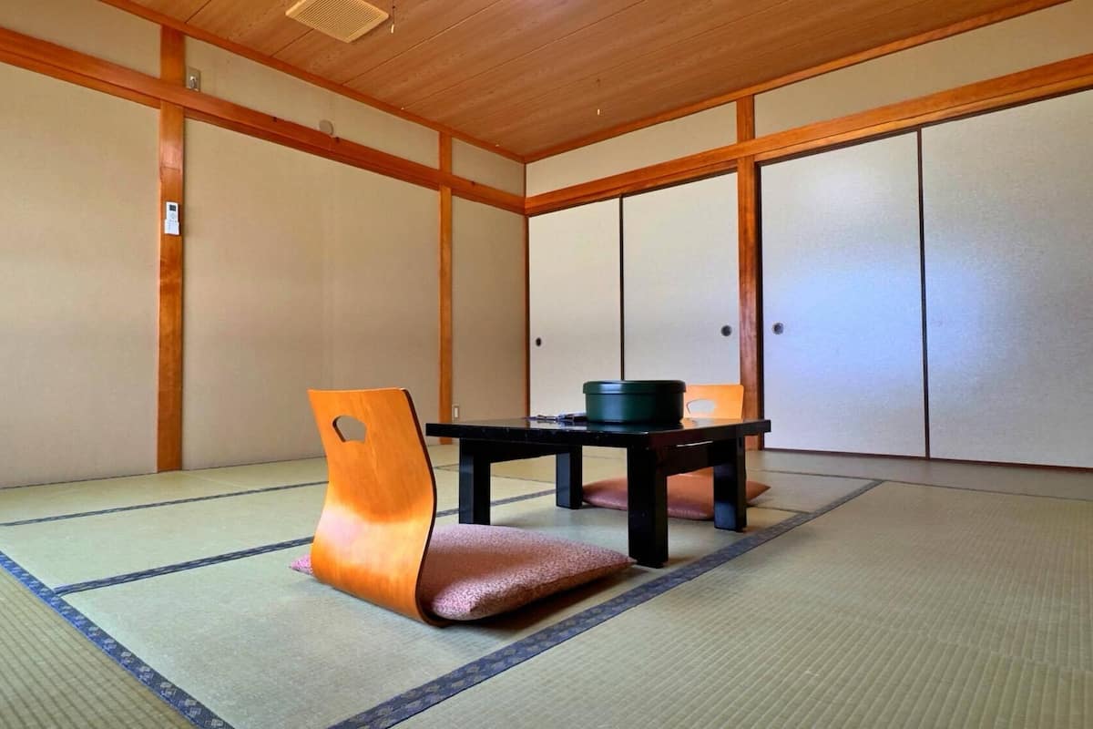 A traditional Japanese room with tatami flooring, a low table, a cushion, and sliding doors.