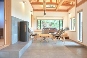 A modern interior with a fireplace, wooden beams, a dining area with chairs, and large windows.