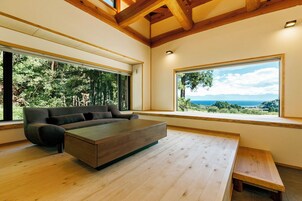 A modern living room with a sofa and coffee table, large windows with a view of the outdoors, and wooden beams on the ceiling.