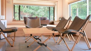 A modern interior with a wooden table and four chairs, large windows with a forest view, and a sofa in the background. - Yuushinan (Nanao)