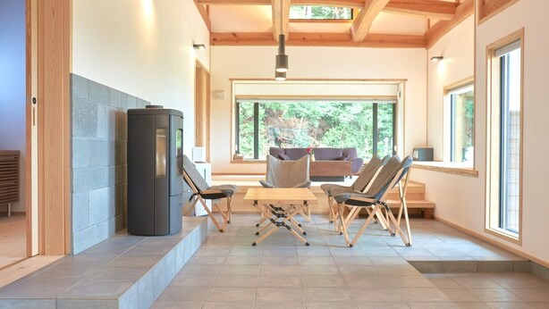 A modern interior with a stone wall, a wood-framed ceiling, a central table with chairs, and large windows. - Yuushinan (Nanao)