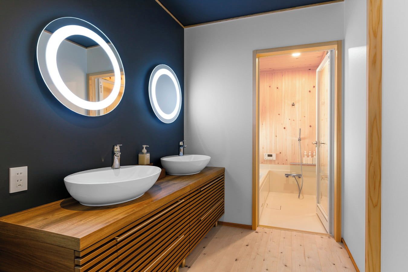 A modern bathroom with two large, oval-shaped sinks, wooden vanity, and a glass-enclosed shower area.