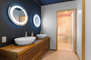 Un baño moderno con dos lavamanos grandes y ovalados, tocador de madera y cabina de ducha con mampara de vidrio.