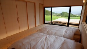 A bedroom with two beds, a sliding door, and a large window with a view of greenery and a distant landscape. - Yuushinan (Nanao)