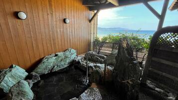 Un interior de madera con una bañera de hidromasaje de piedra, paredes de madera y vista al mar.