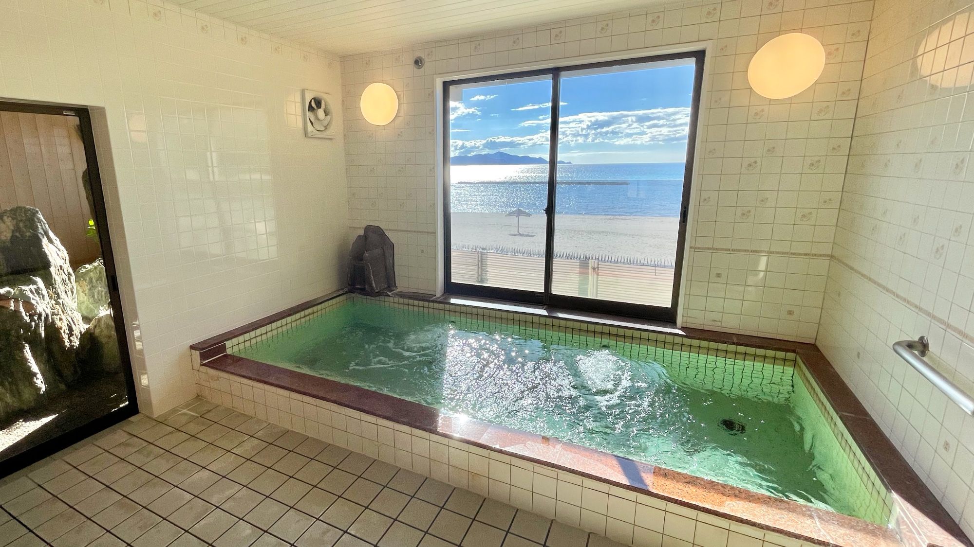 Una habitación con un ventanal grande, una bañera y un ventilador en la pared.