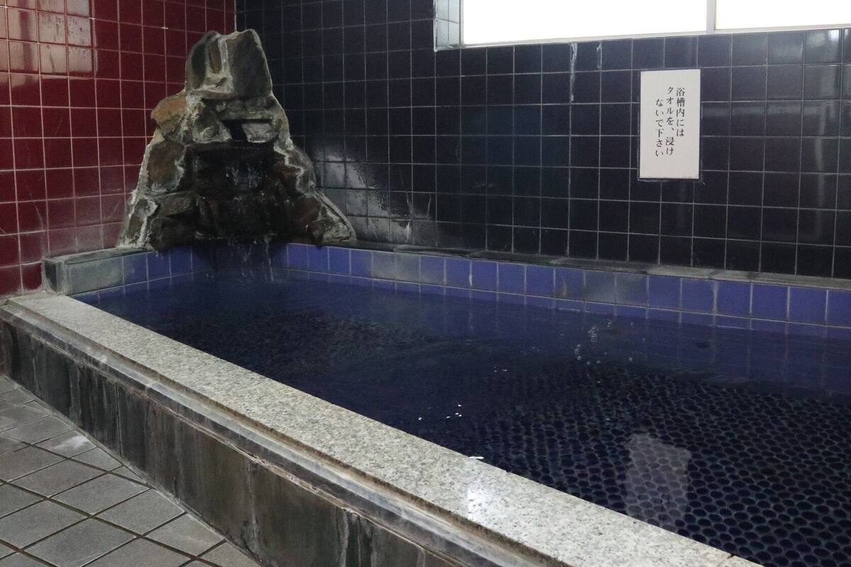 A blue tiled pool with a stone feature, a tiled wall, and a sign.