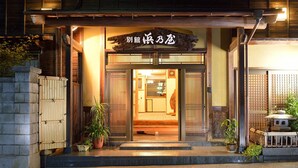 A traditional Japanese entrance with a wooden sign, a stone lantern, and potted plants. - Ryokan Hama no Ya (Kyotango)