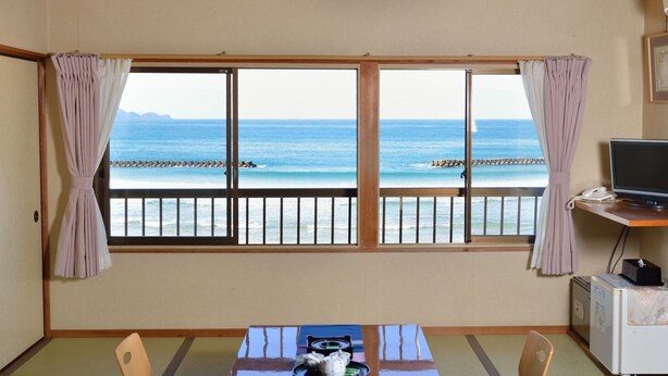 A room with a view of the sea, a table with items, a chair, a TV, and a refrigerator. - Ryokan Hama no Ya (Kyotango)