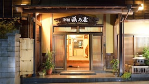 A traditional Japanese entrance with a wooden sign, a stone lantern, and potted plants. - Ryokan Hama no Ya (Kyotango)
