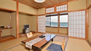 A traditional Japanese room with tatami flooring, a low table, a television, and a view of the sea through large windows. - Ryokan Hama no Ya (Kyotango)