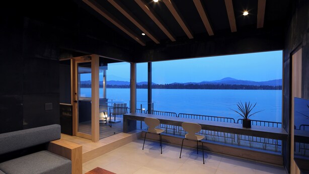 A modern interior with a sofa, a wooden table, and a balcony with a view of a lake and mountains. - Torch Amano-hashidate (Yonezawa)